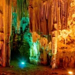 Young woman touching huge stalactites in colorful Melidoni Cave